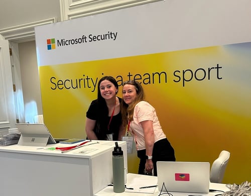 Two women stand behind a desk at a Microsoft Security event.