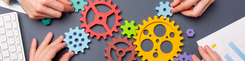 Several hands holding gears and putting them together like a puzzle.