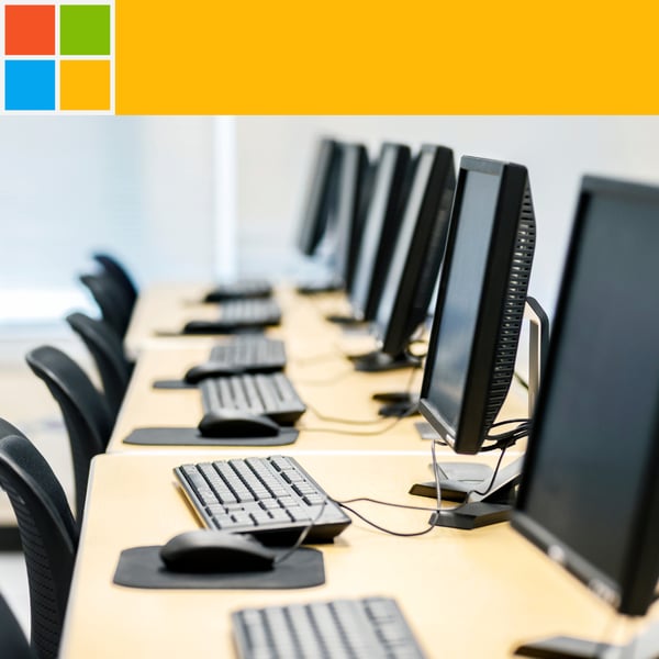 A photograph of a bank of computers on a long desktop, receding to the distance, above is a Microsoft logo