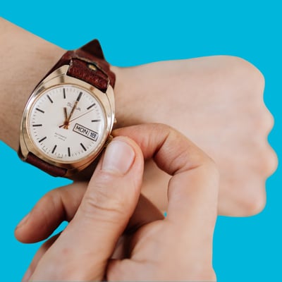An old style wristwatch is on a person's wrist. The other hand is winding the dial to change the time or date.