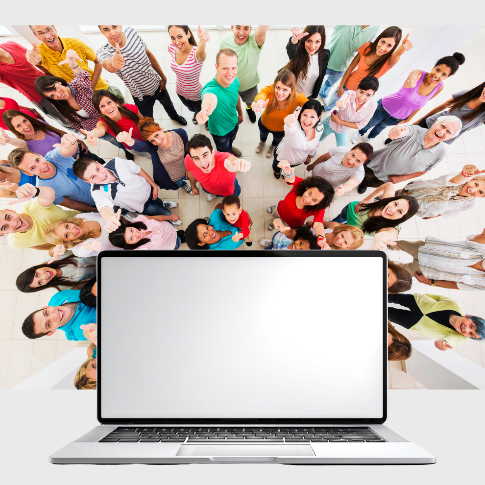 A blank laptop computer at the forefront with a photograph of lots of people behind it pointing upwards towards the camera