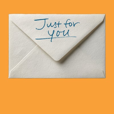 A plain envelope on an orange background with handwriting reading 'Just for you' on the back