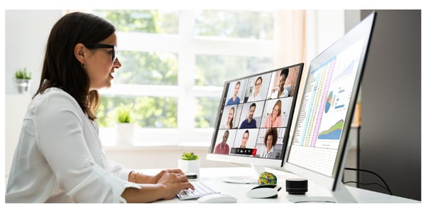 A white lady with shoulder length brown hair types on a keyboard whilst watching a webinar on her screen