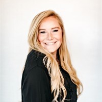 A white woman with long blonde hair smiles broadly at the camera. She is wearing a black top.