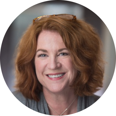 A close up of a red headed lady with glasses on top of her head. She is smiling broadly.