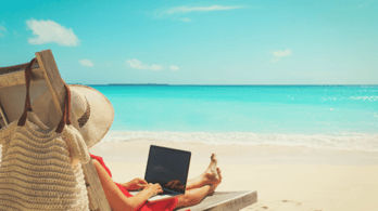 Woman on beach with laptop open - working remotely.